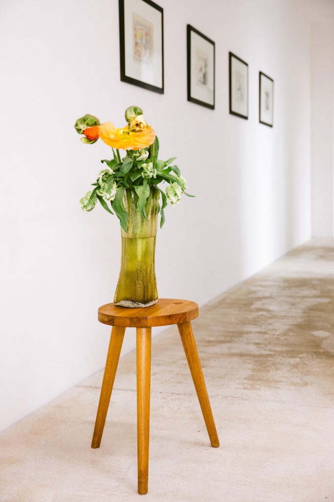 Der Hocker von Buchholzberlin ist aus geölter Eiche, darauf eine olivgrüne Vase mit Mohnblumen und Tulpen.