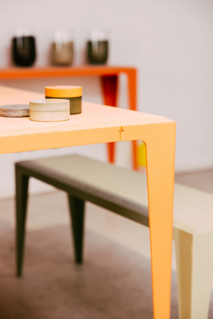 Die hochwertigen Oberflächen von Wye Design's Möbeln aus Neolignplatten kann man abschleifen. Hier Tische und eine Bank in Grau und Korallrot.